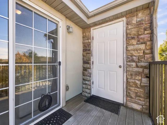 Private balcony featuring natural stone veneer siding, sliding glass door, six-panel exterior door, wood-plank decking, and metal railing