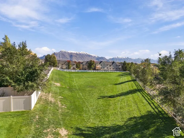 Expansive grassy lot featuring perimeter white vinyl fencing and a backdrop of snow-capped mountains
