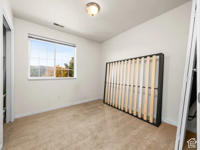 Neutral-toned carpeting, single-pane sliding window, ceiling-mounted light fixture, and bi-fold closet doors