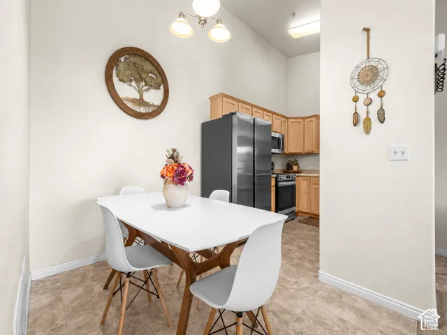 Kitchen area featuring light-toned wood cabinetry, stainless steel appliances, neutral stone-finish flooring, and high ceilings