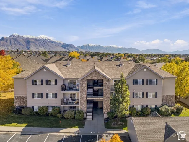 Multi-story building exterior featuring stone masonry accents, horizontal siding, asphalt shingle roofing, shutter-trimmed windows, and mountain range scenery