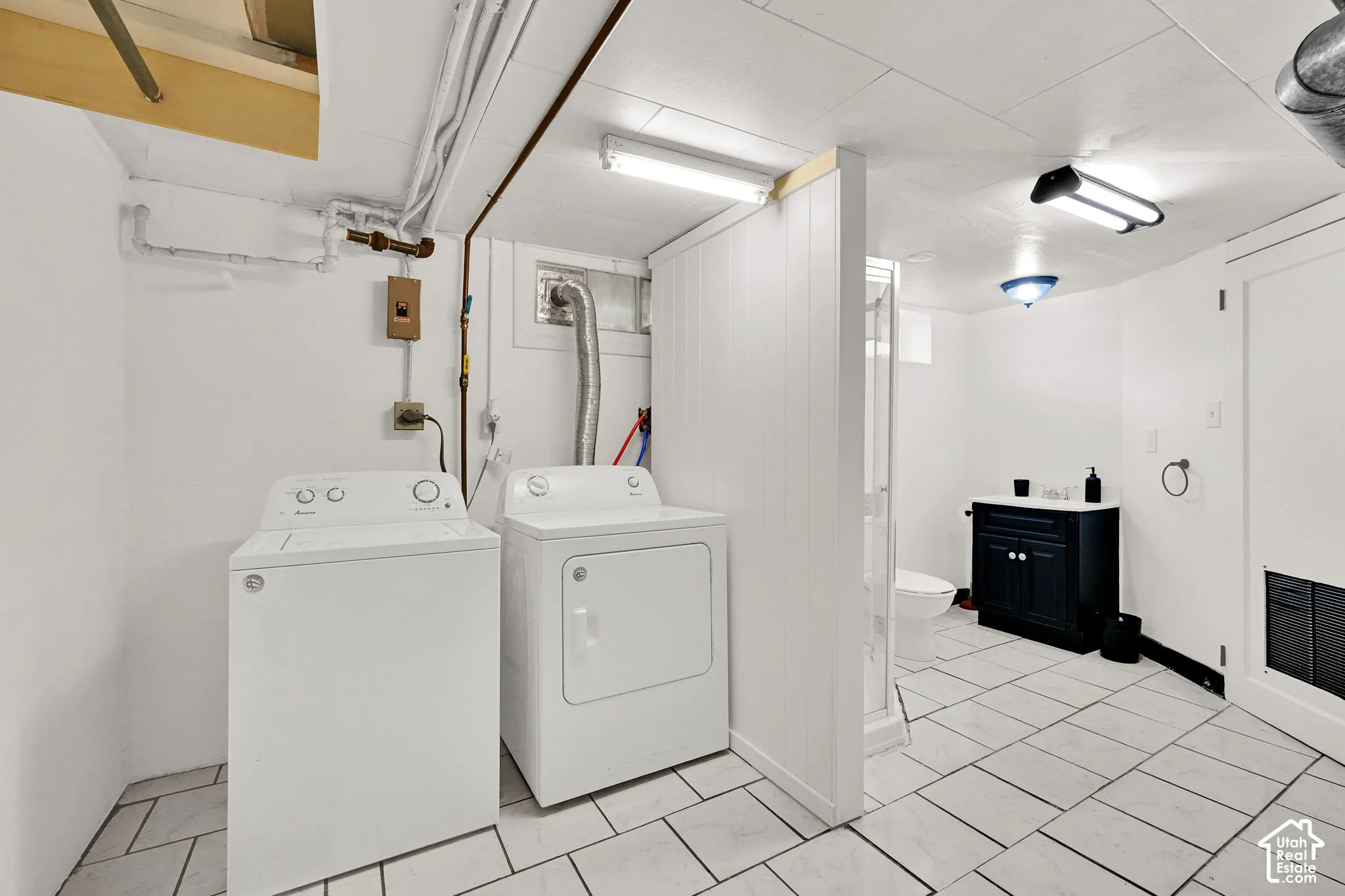 Utility space featuring white tile flooring, vertical panel wall partition, enclosed shower stall, and dark-finish vanity cabinet with a white countertop
