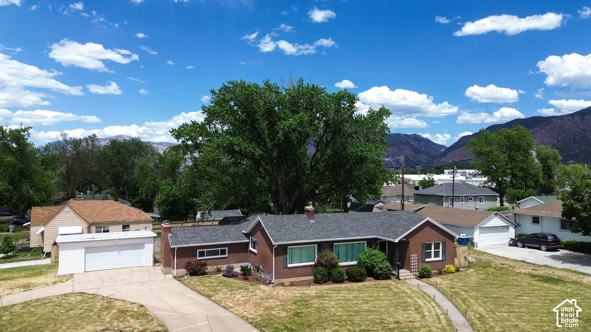 Single-story brick exterior featuring an attached garage, asphalt shingle roof, concrete driveway, and mountain backdrop