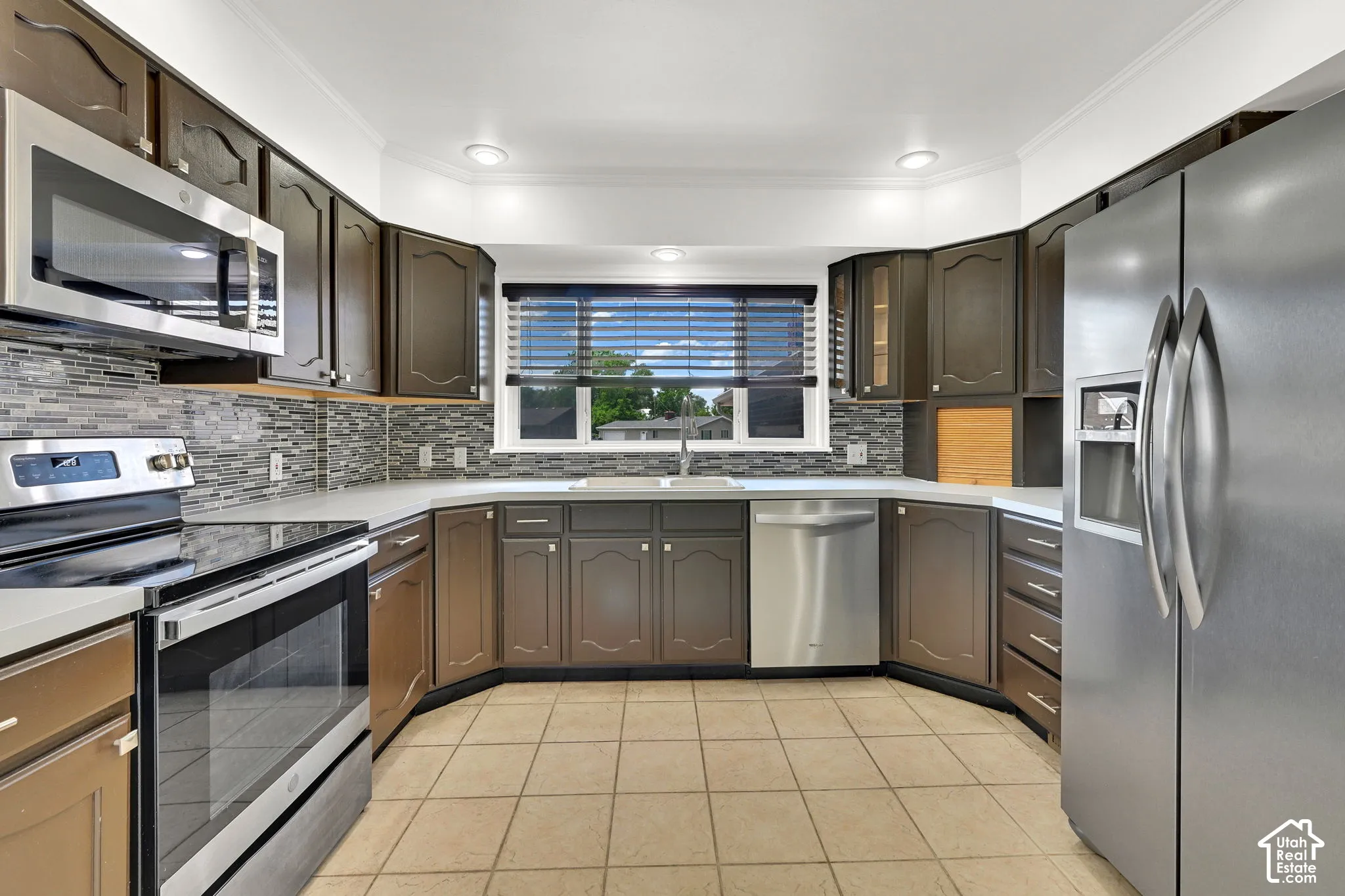Kitchen featuring dark-finish cabinetry, stainless steel appliances, multi-toned tile backsplash, recessed lighting, and tile flooring
