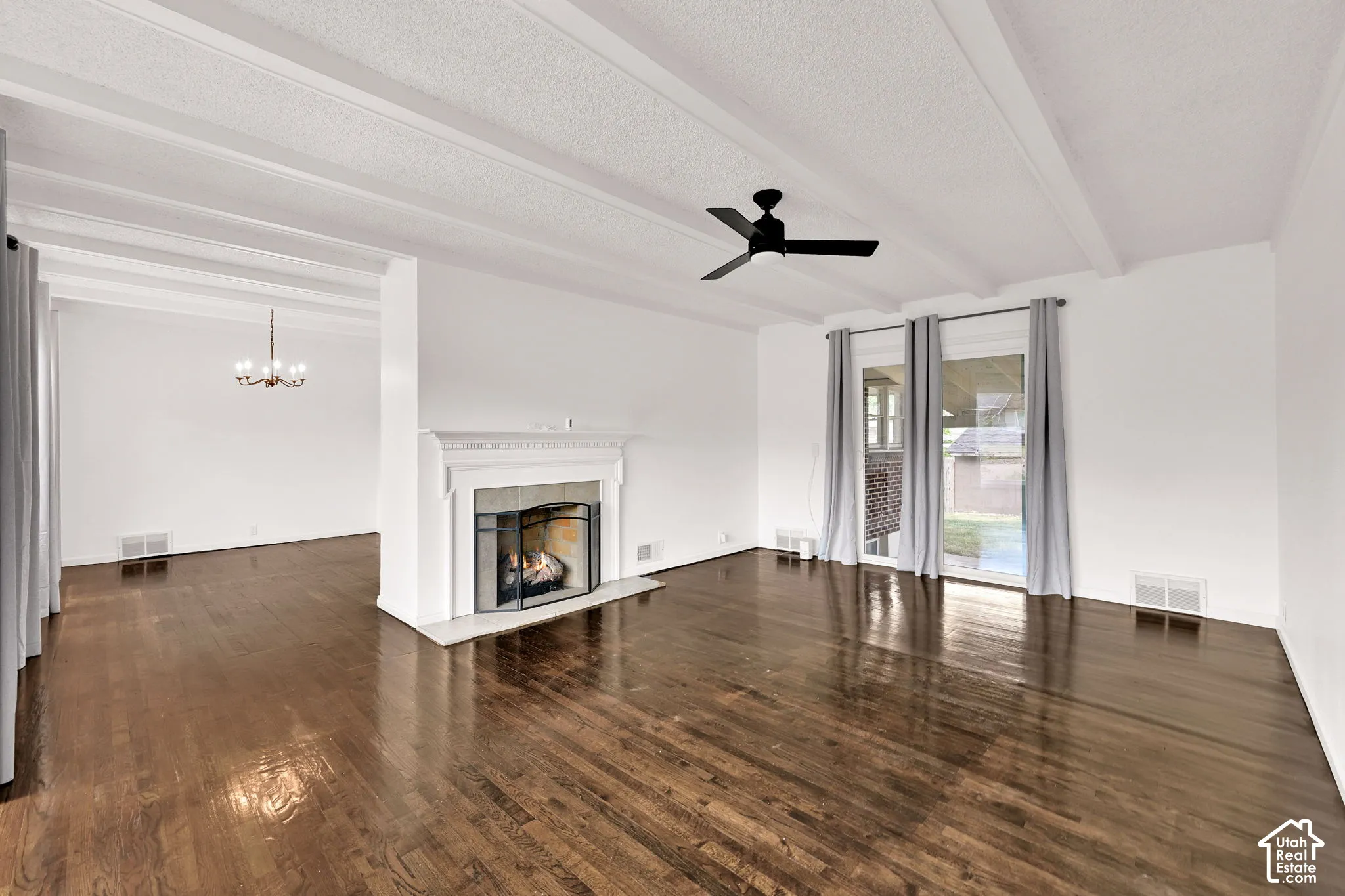 Living space featuring exposed ceiling beams, wood-finish flooring, a central fireplace with a decorative mantel, and a sliding glass door