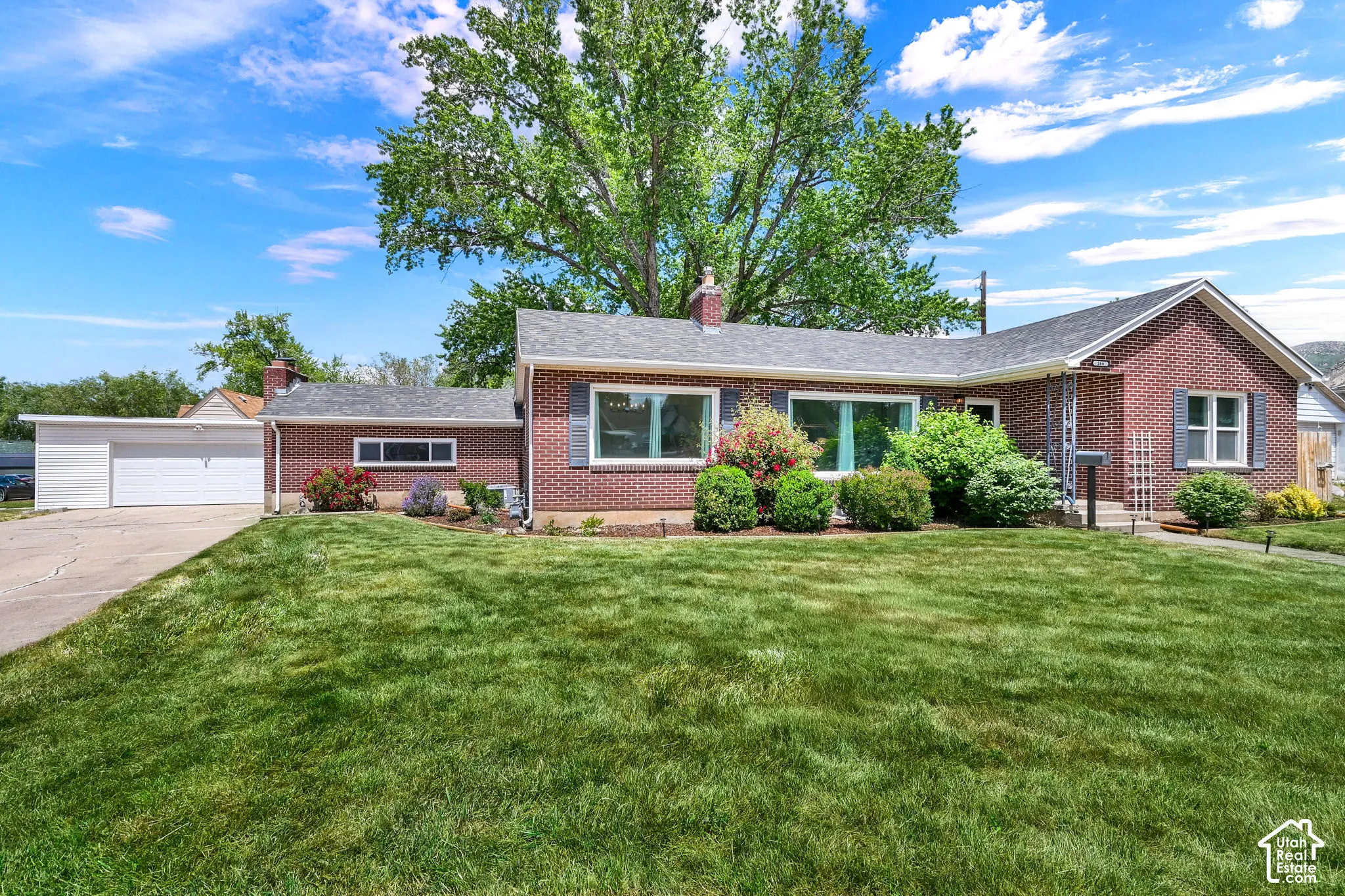 Single-story brick exterior featuring a multi-gable roofline, attached garage, large front lawn, and mature landscaping