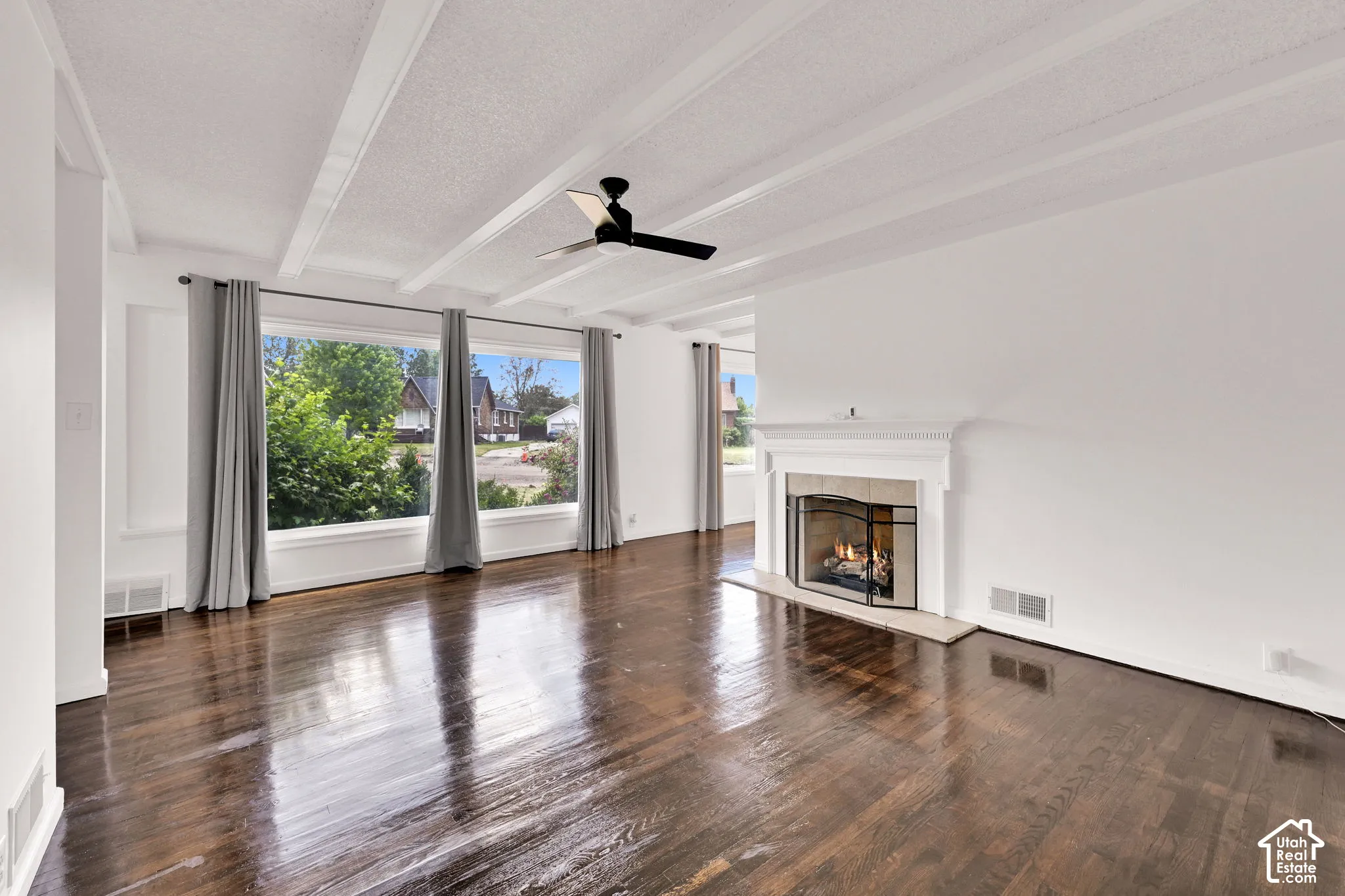 Living space featuring wood-finish flooring, white exposed beam ceiling, large picture window, and a fireplace with a stone-surround mantle