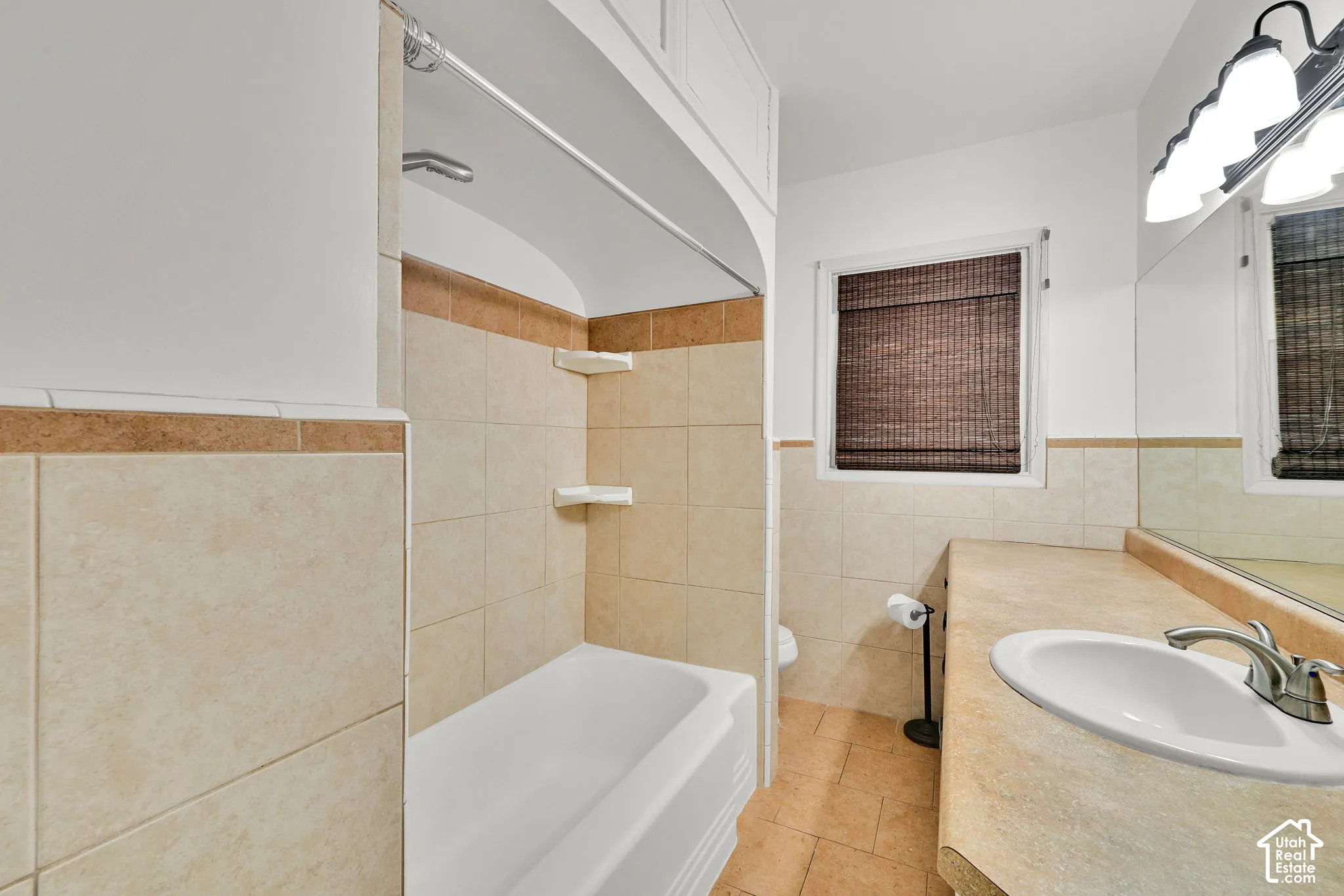 Bathroom featuring a tub-shower combination with tiled surround, built-in recessed shelving, integrated vanity countertop with an undermount sink, and wall-mounted vanity lighting