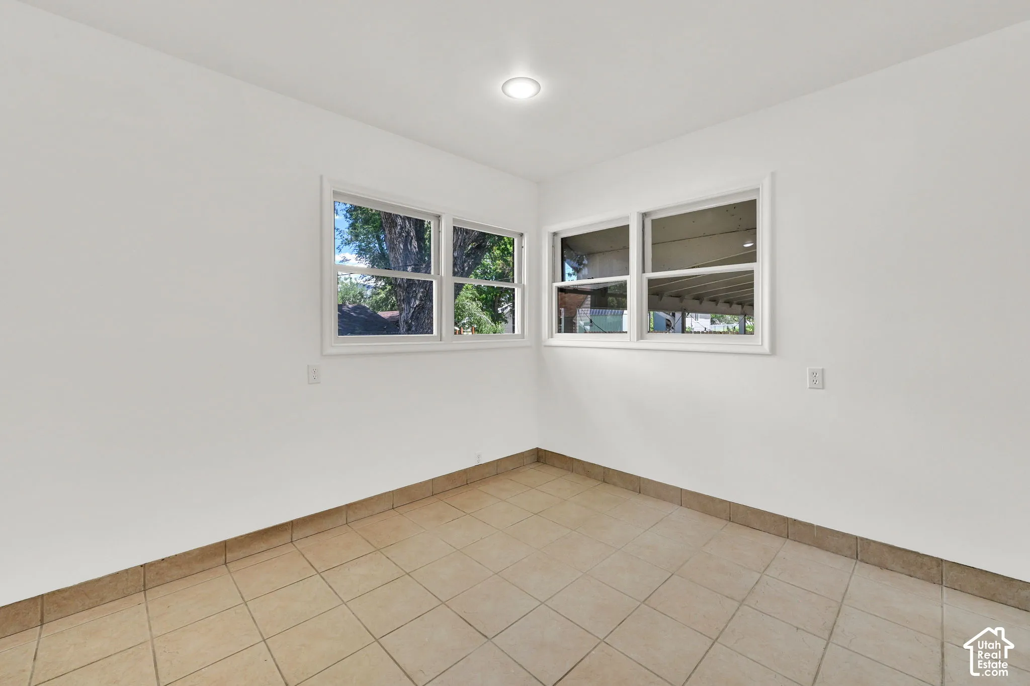 Neutral interior space featuring ceramic tile flooring, crisp white walls, recessed ceiling lighting, and multiple windows with white trim