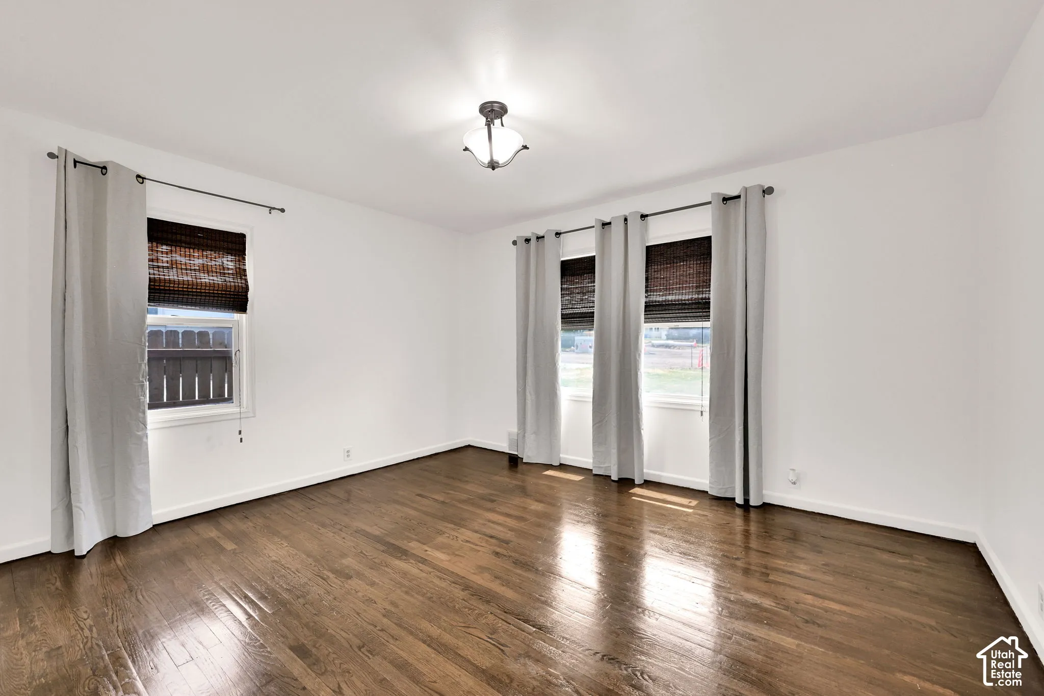 Interior space featuring dark wood-finish flooring, neutral wall tones, multi-pane windows, and a central ceiling-mounted light fixture