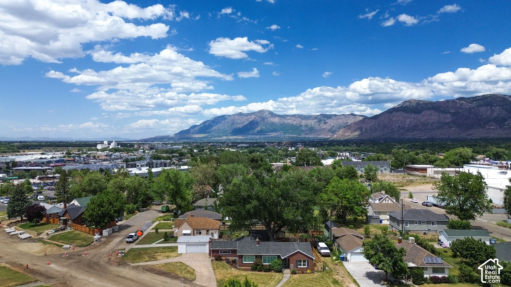 Aerial perspective of a single-story residence featuring brick exterior cladding, asphalt shingle roofing, and an attached garage, set against a prominent mountain backdrop