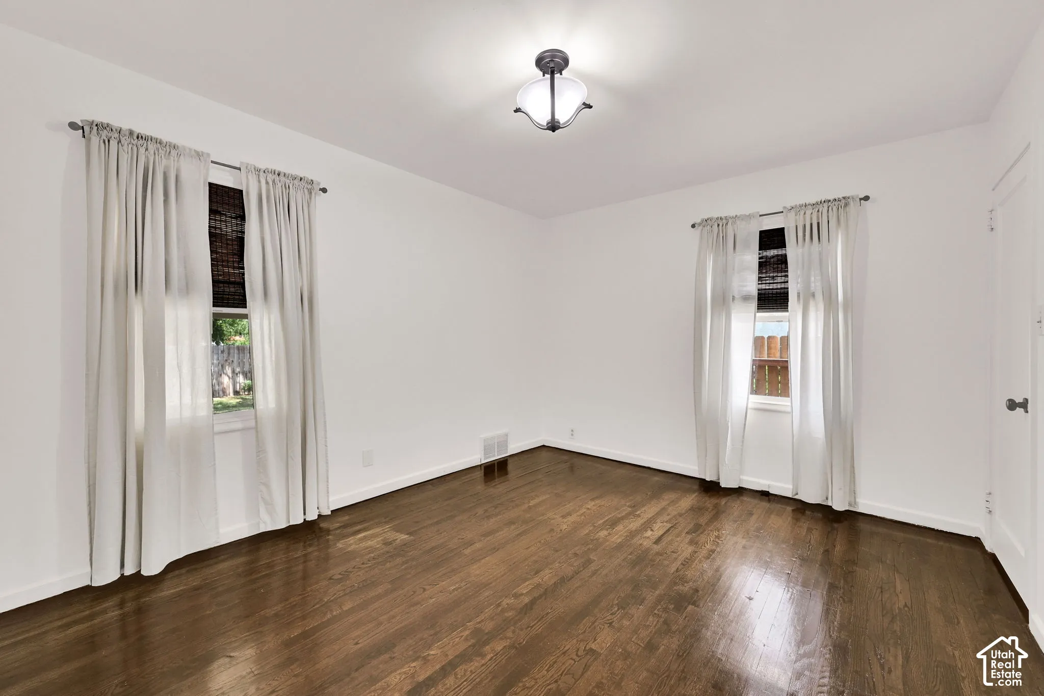 Room featuring wood-finish flooring, two windows, and a flush-mount ceiling light fixture