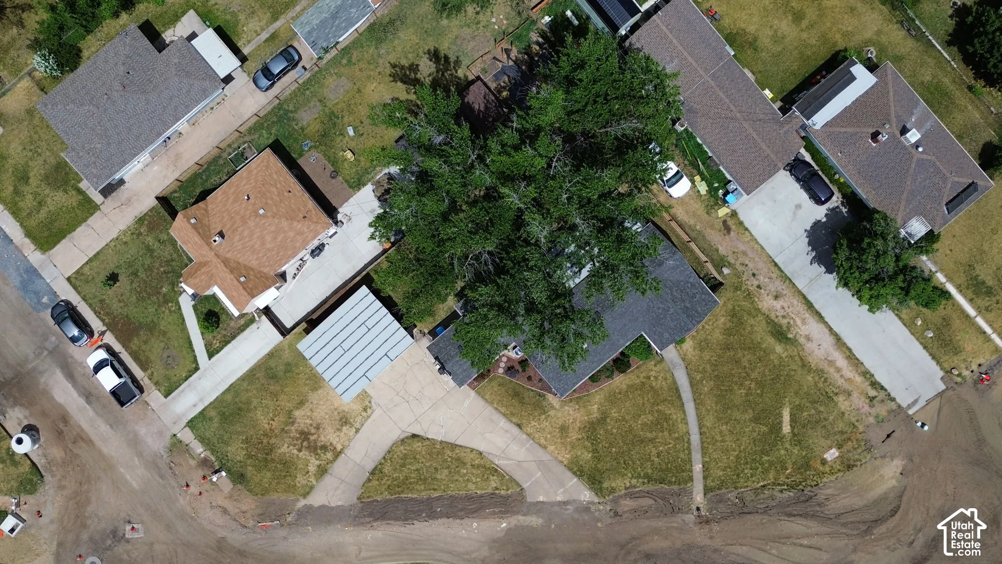 Aerial view of property featuring a shingled roof, paved driveway, carport, and mature trees