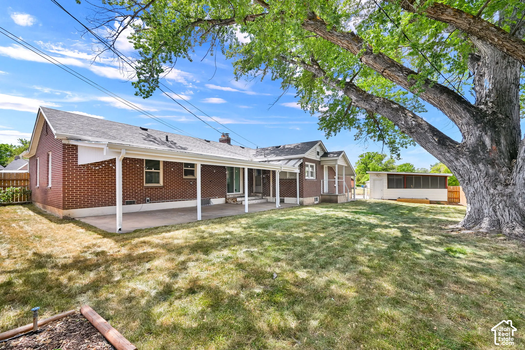 Brick exterior residence featuring a covered patio, expansive lawn, mature trees, and a detached structure
