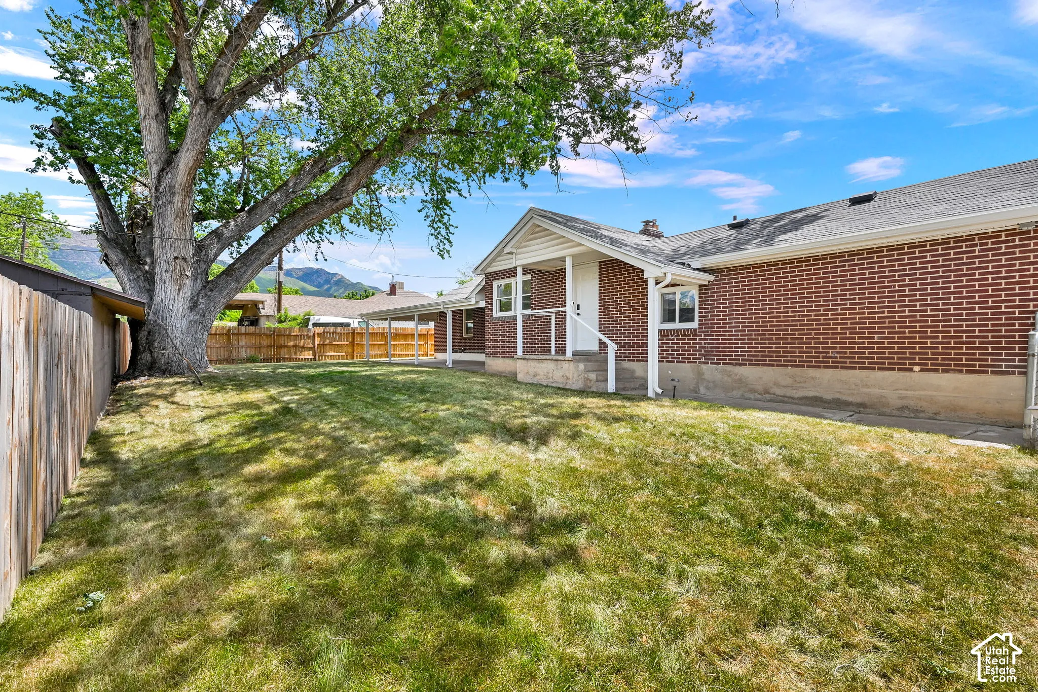 Exterior featuring red brick masonry, a covered patio structure, a large mature tree, and wood-panel fencing