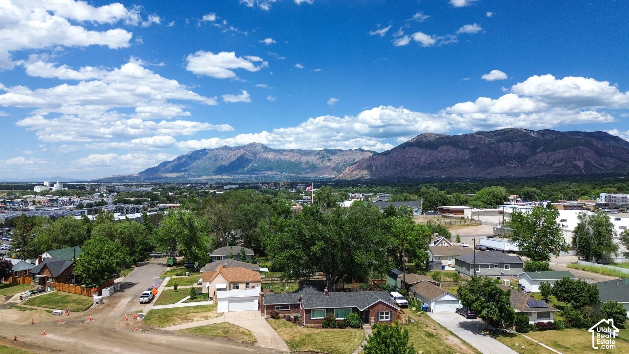 Aerial perspective featuring a single-story brick residence with an attached two-car garage, mature landscaping, and prominent mountain backdrop