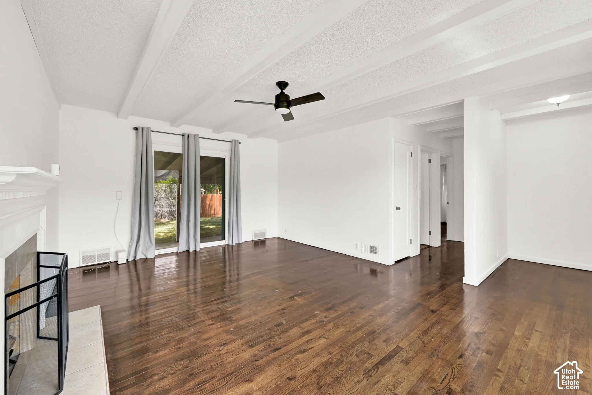 Open living area featuring wood-finish flooring, exposed ceiling beams, a masonry fireplace with a stone hearth, and sliding glass doors
