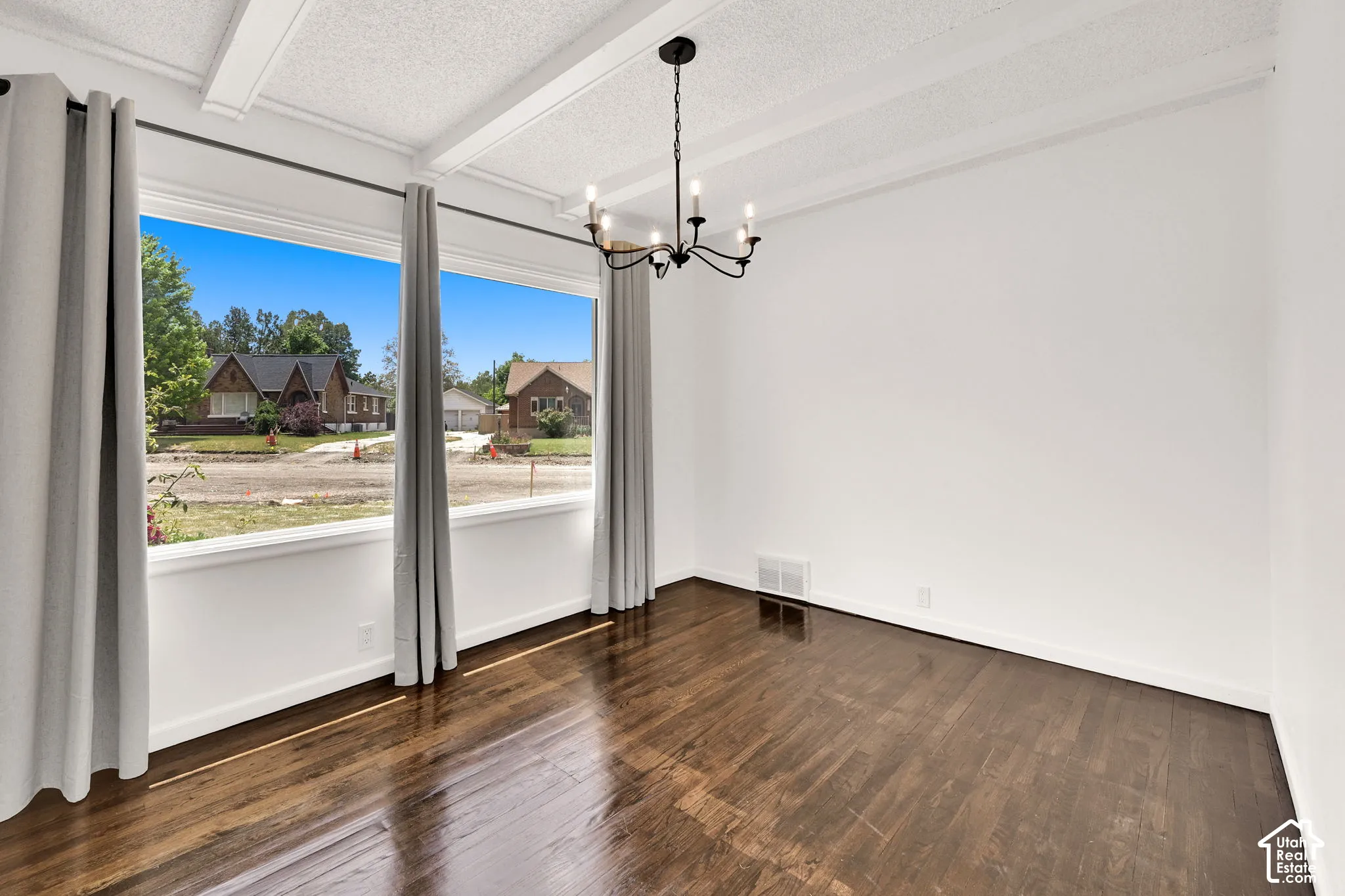 Room interior featuring wood-finish flooring, exposed ceiling beams, and a black metal chandelier