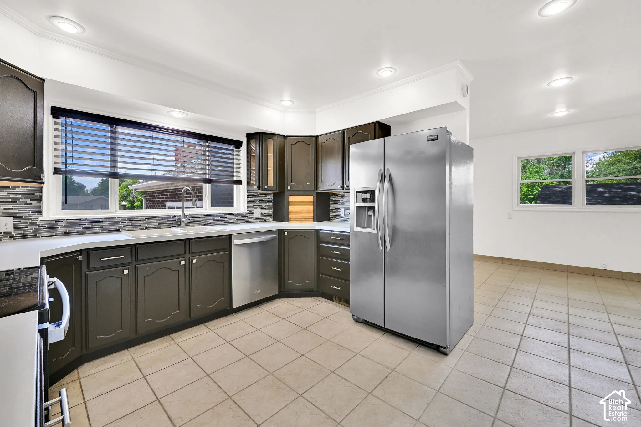 Kitchen featuring dark-finish cabinetry, stainless steel appliances, multi-toned decorative backsplash, and neutral tile flooring