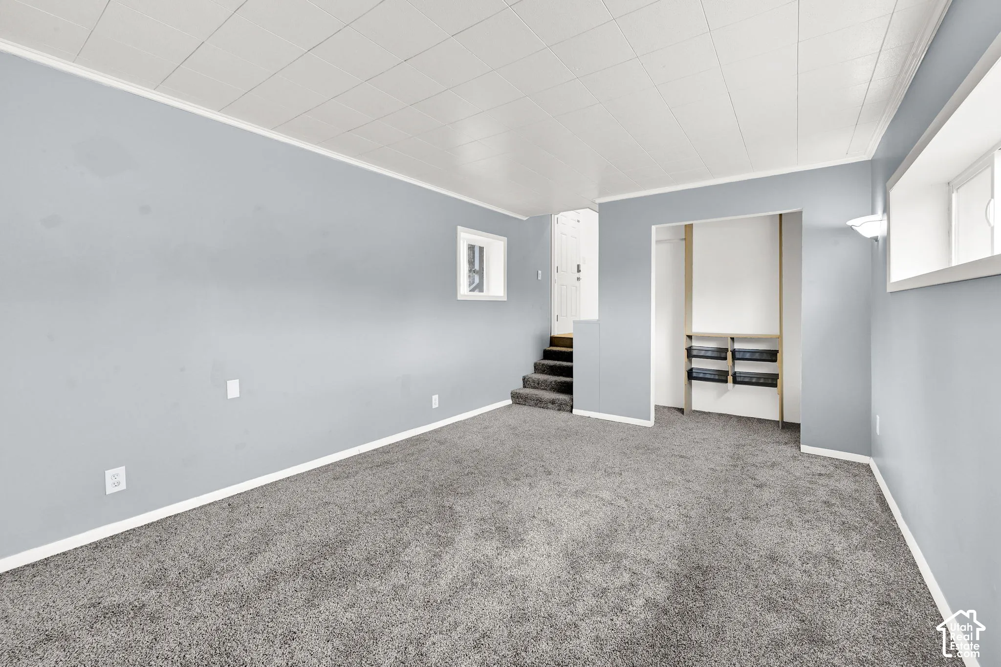 Interior space featuring wall-to-wall carpeting, ceiling tiles, built-in shelving, and dual recessed windows