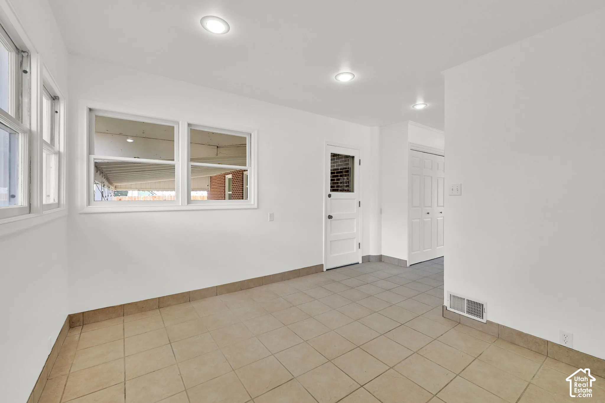 Neutral interior featuring tile flooring, recessed ceiling lighting, a door with a glass pane, and multi-pane windows