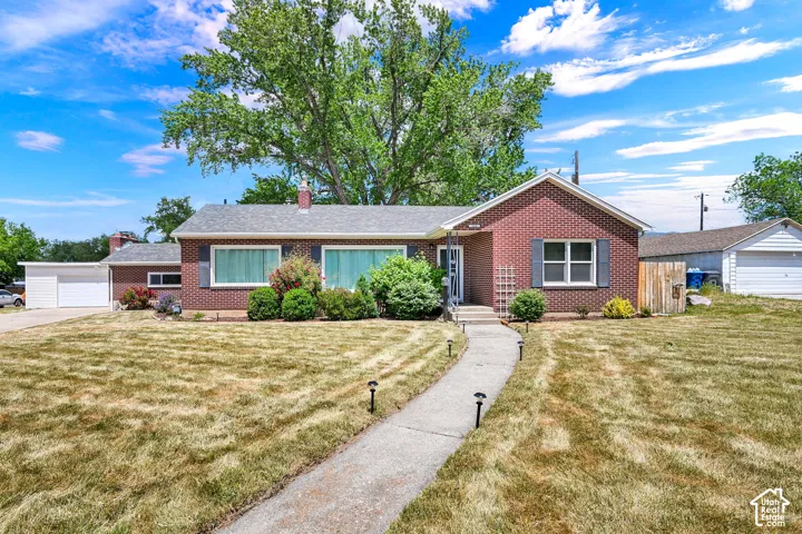 Red brick exterior featuring a multi-gabled roofline, concrete walkway, detached garage, and mature landscaping