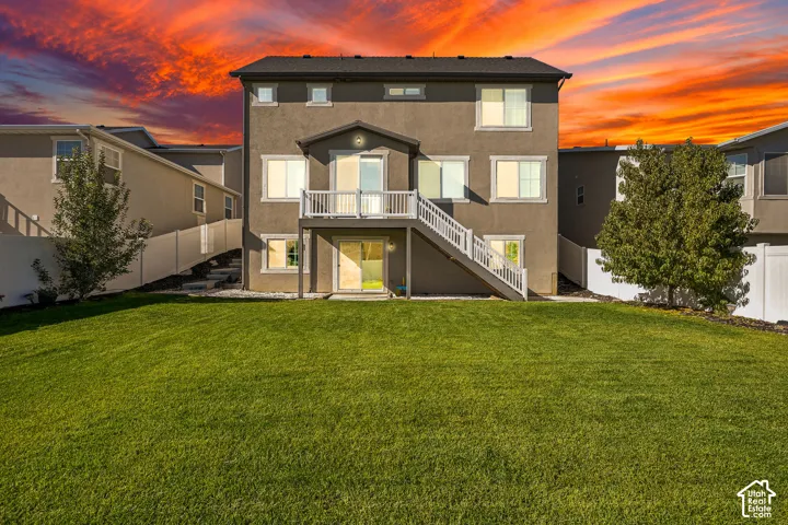 Two-story stucco exterior featuring a raised deck with white railing, staircase, sliding glass doors, and a manicured lawn