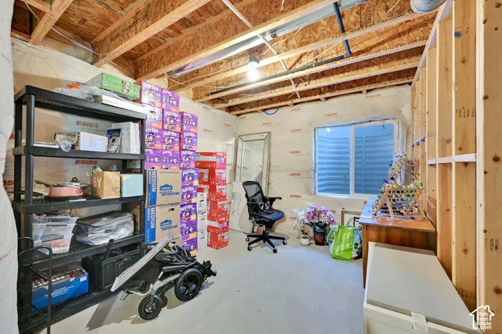 Unfinished room featuring exposed wooden joists, insulated walls, concrete flooring, and an egress window with a window well