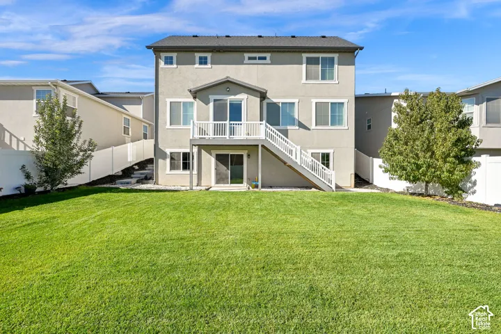 Exterior elevation featuring a stucco facade, elevated wood deck with white railing, stone staircase, and a fenced backyard with lawn