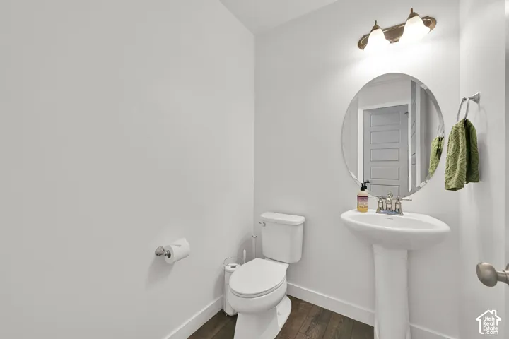 Powder room featuring a pedestal sink, polished chrome faucet, round mirror, two-light fixture, and wood-finish flooring