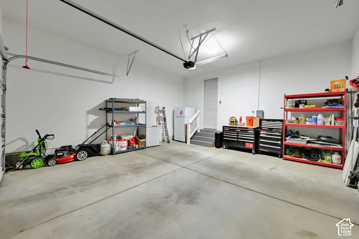 Attached garage featuring finished walls, concrete flooring, and a dedicated staircase
