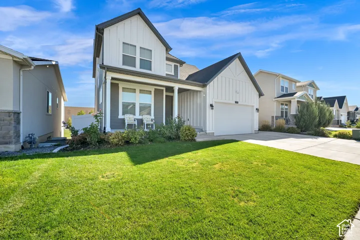 Two-story farmhouse-inspired exterior featuring vertical board-and-batten siding, a covered front porch with column supports, a paved driveway, and an attached two-car garage