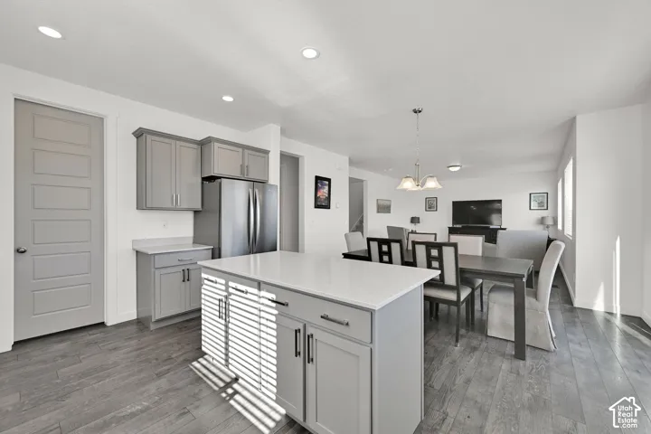 Kitchen featuring gray cabinetry, a central island with a solid surface countertop, wood-finish flooring, recessed lighting, and a multi-light chandelier