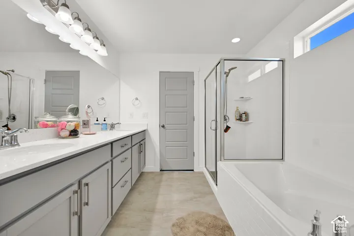 Bathroom featuring a dual-sink vanity with light-colored countertops, walk-in glass-enclosed shower, separate soaking tub, and tile-finish flooring