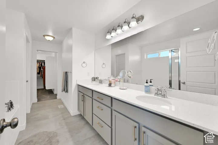 Dual vanity with light-grey cabinetry, light-toned stone-surface countertop, full-width mirror, and polished-finish hardware, complemented by tile flooring