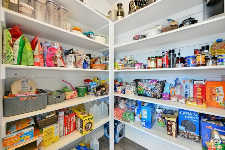 Walk-in pantry featuring white shiplap wall paneling, multiple tiers of built-in shelving, and wood-finish flooring