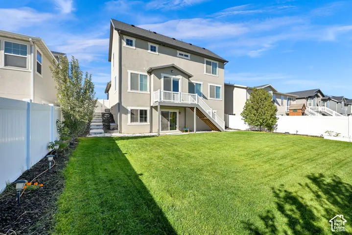 Rear elevation featuring a multi-level exterior, raised wooden deck with white railing, stone staircase, white vinyl fencing, and a manicured lawn