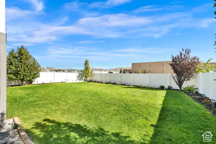 Expansive backyard featuring a level lawn, white vinyl perimeter fencing, and mature trees