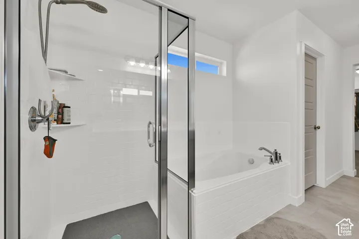 Walk-in shower with a framed glass enclosure, white subway tile surround, and built-in shelving, complemented by a separate soaking tub with tiled surround and horizontal light fixture