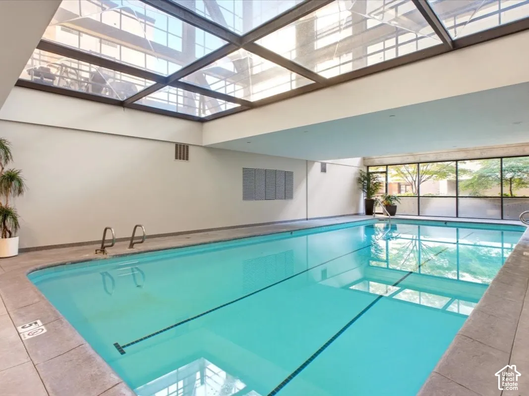 Indoor pool area featuring an expansive glass-paneled skylight, tile surround, recessed lighting, and wall-to-wall windows