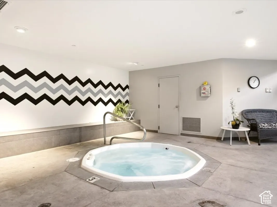 Indoor spa featuring an octagonal jetted tub, stainless steel grab bar, concrete-finish flooring, and recessed ceiling lighting