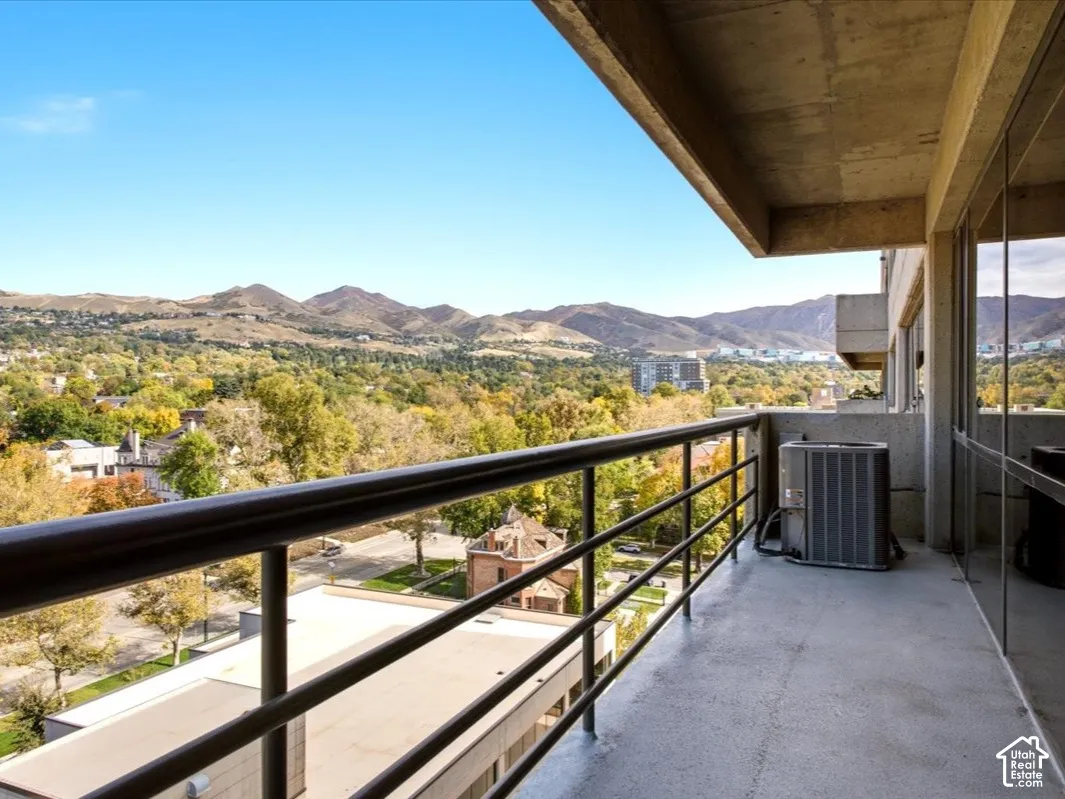 Covered balcony featuring concrete flooring, full-length glass wall panels, a metal railing, and extensive mountain scenery