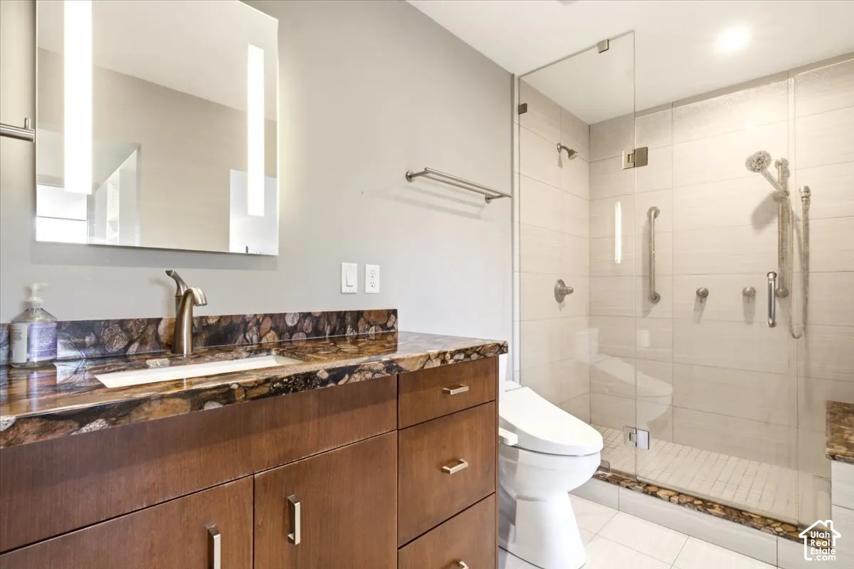 Bathroom featuring a wood-finish vanity with a stone-surfaced countertop, integrated rectangular sink, wall-mounted illuminated mirror, and a walk-in shower with a glass enclosure and dual shower heads