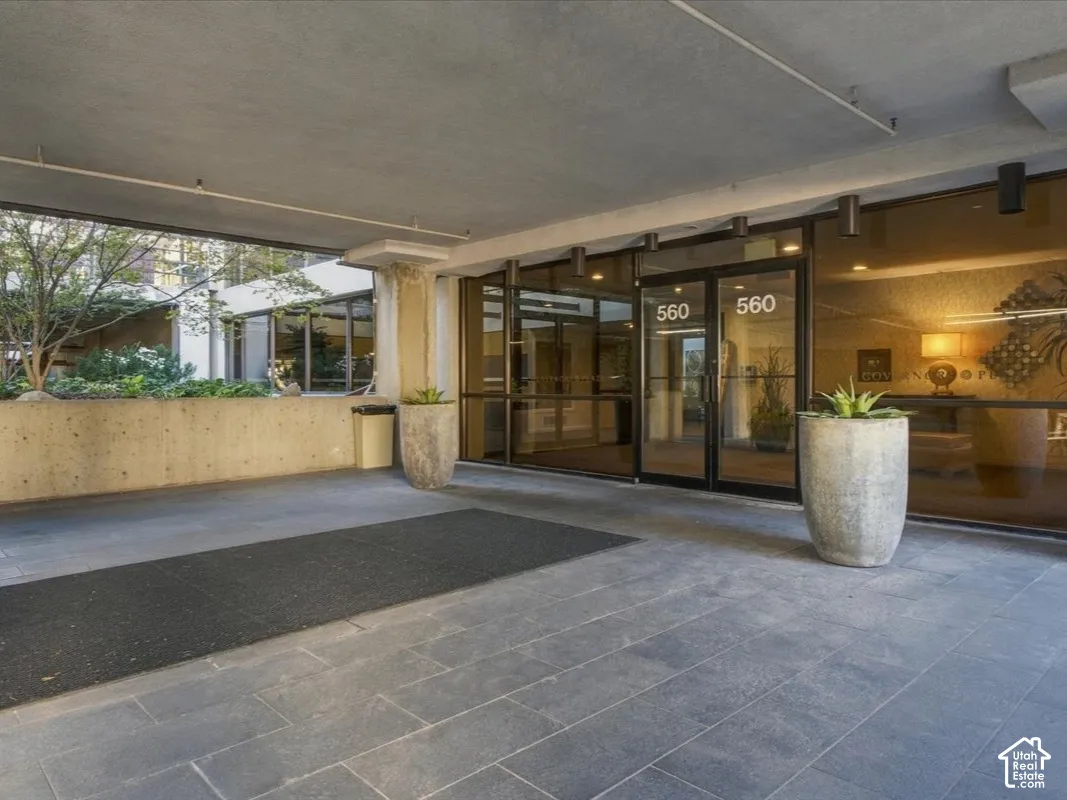 Covered building entrance featuring large-format stone floor tiles, floor-to-ceiling glass paneling, recessed ceiling lighting, and built-in concrete retaining walls