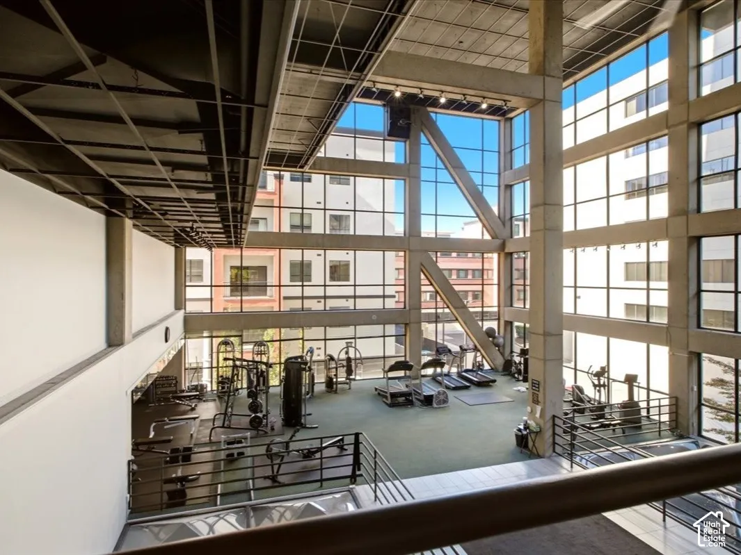 fitness facility featuring floor-to-ceiling glass curtain walls, industrial concrete structural columns, exposed metal ceiling joists, and integrated track lighting