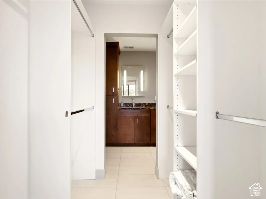 Walk-in closet featuring white built-in shelving and dual hanging rods, ceramic tile flooring, and dark wood cabinetry with a stone countertop