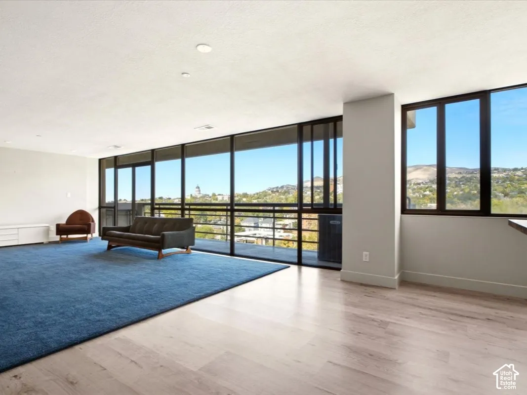Floor-to-ceiling windows with dark metal frames, light-toned wood-finish flooring, and recessed ceiling lighting