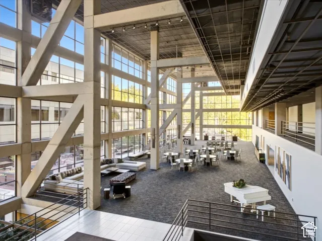 Expansive multi-level interior featuring floor-to-ceiling glass paneling, exposed structural steel beams, high-volume ceilings with industrial-style overhead grid, and metallic railings