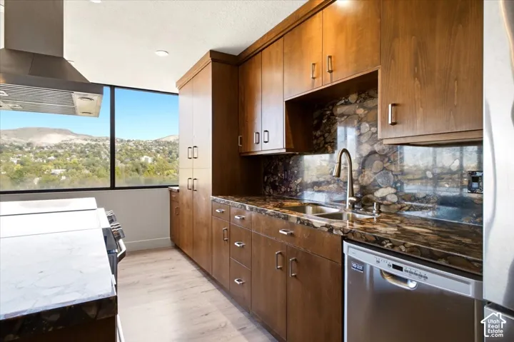 Kitchen featuring wood cabinetry, stone-surface countertops, stone-tile backsplash, stainless steel appliances, and large-format windows with mountain scenery