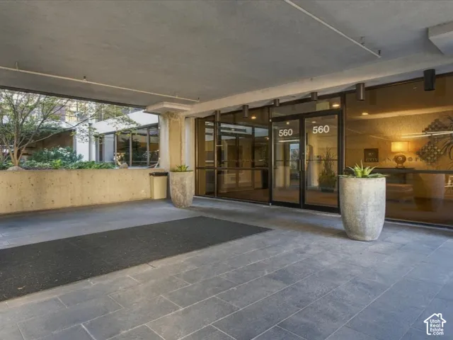 Covered building entrance featuring large-format stone floor tiles, floor-to-ceiling glass paneling, recessed ceiling lighting, and built-in concrete retaining walls